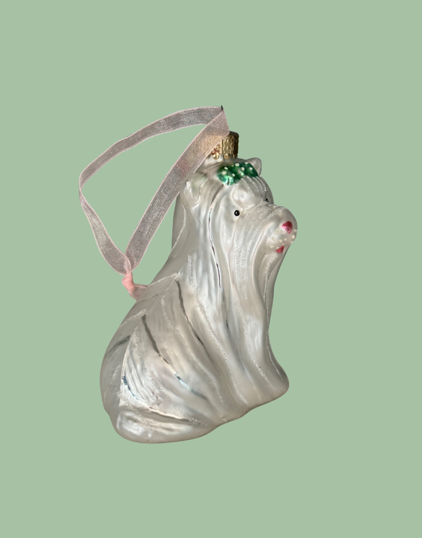 A vintage-style West Highland Terrier Christmas ornament made of textured, translucent white glass with a pink ribbon hanger, a small green bow, and a gold top cap, set against a solid sage green background.