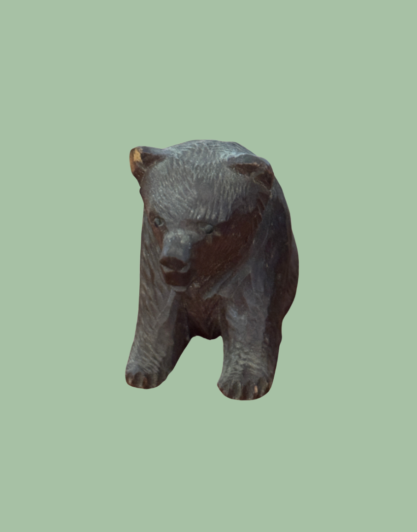 A small carved wooden bear figurine with dark brown and black tones, shown against a solid pale green background.