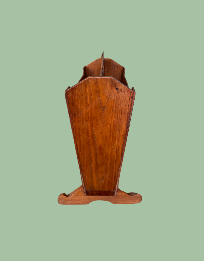 A vintage wooden display stand or bookcase with a warm reddish-brown finish, shown against a solid sage green background.
