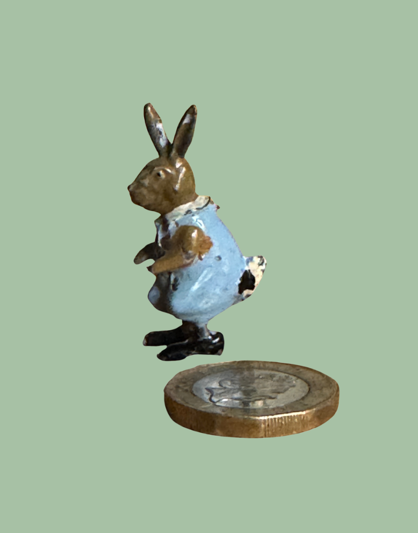 Tiny lead metal painted rabbit figurine next to one pound coin for scale