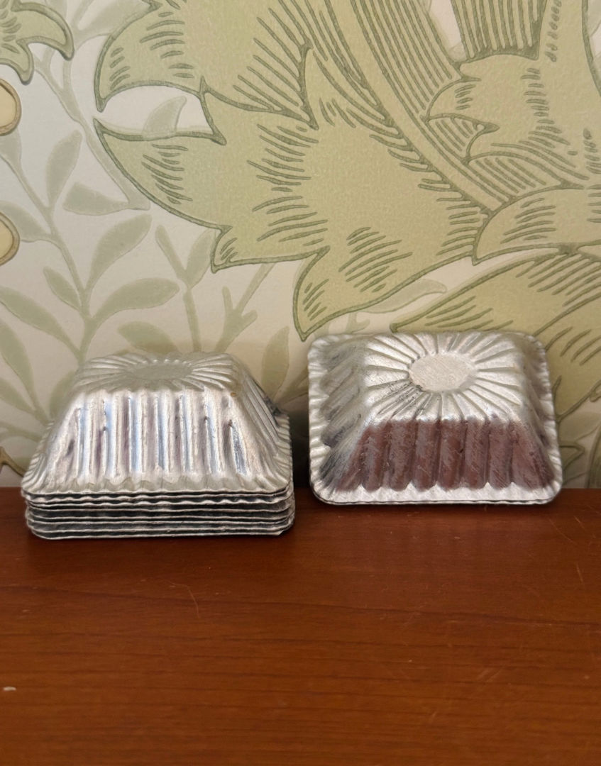 Ten vintage aluminium chocolate moulds displayed together showing rectangular shape, scalloped edges and aged patina