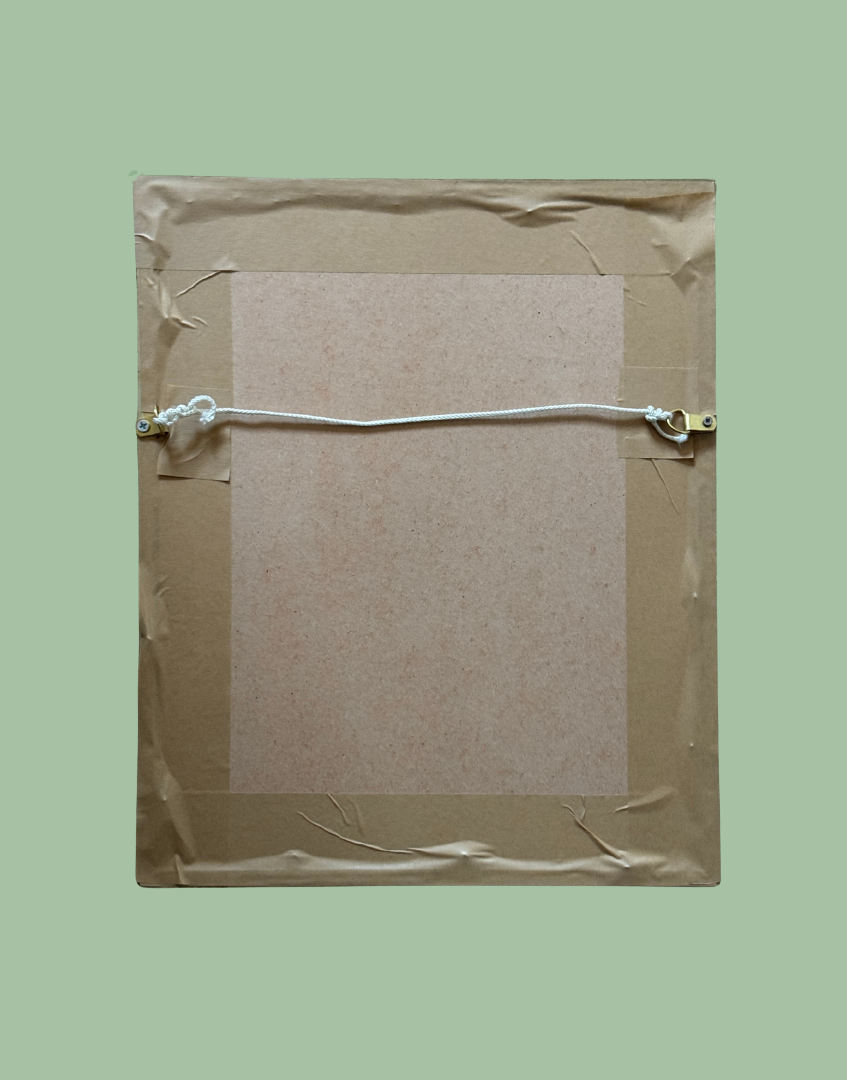 The back of a square framed picture frame, showing a brown kraft paper backing, a central tan insert, and a white hanging cord with brass grommets, set against a solid sage green background.