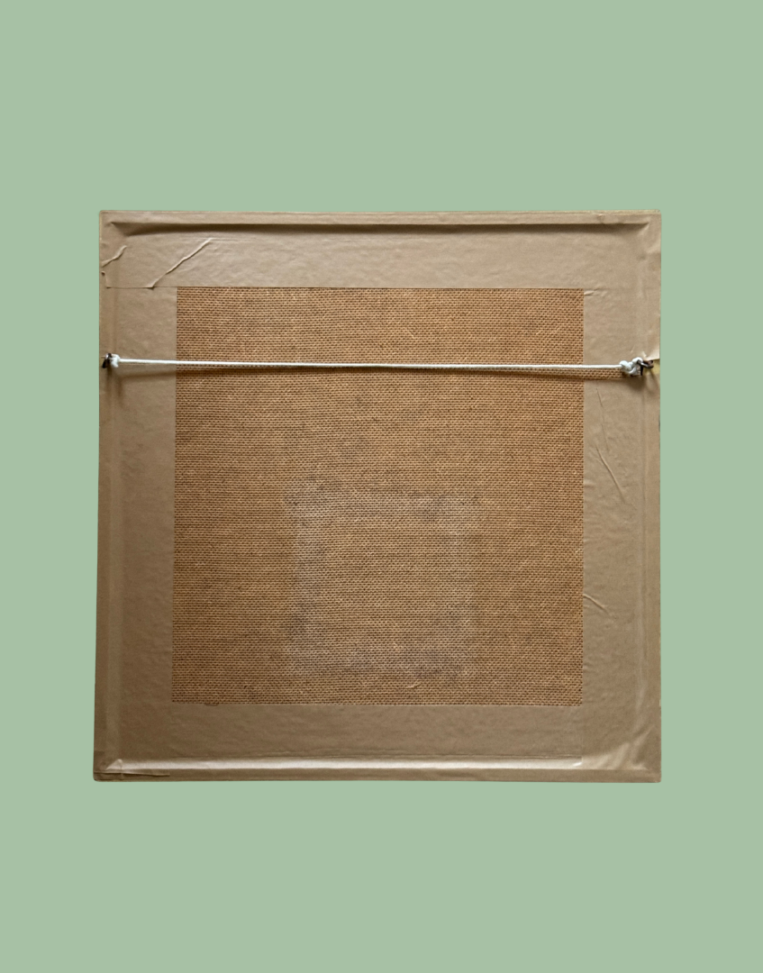 The back of a square framed artwork or print, showing a tan woven mat, a beige border, and a horizontal hanging cord against a solid sage green background.