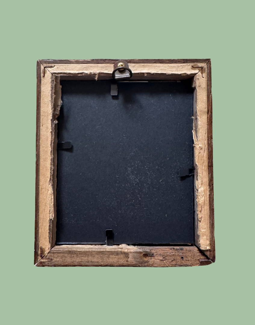 The back of a rustic wooden picture frame with a black backing board and metal hanging hardware, shown against a solid sage green background.