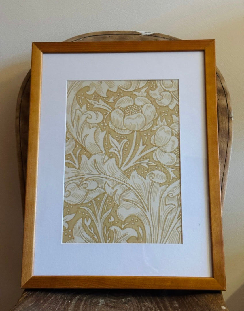 A framed art print featuring a classic William Morris floral pattern in beige and white, set within a light brown wooden frame with a wide white mat board.
