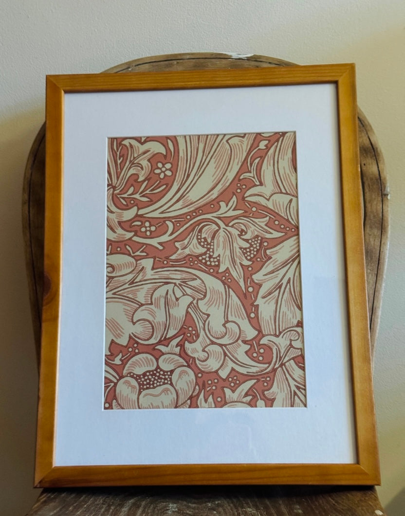 Framed art print featuring an Art Nouveau floral pattern in terracotta red and cream, set in a light oak wood frame with a white mat board.