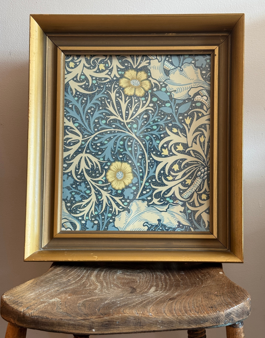 Vintage framed William Morris print styled on an antique wooden chair in a rustic cottage setting