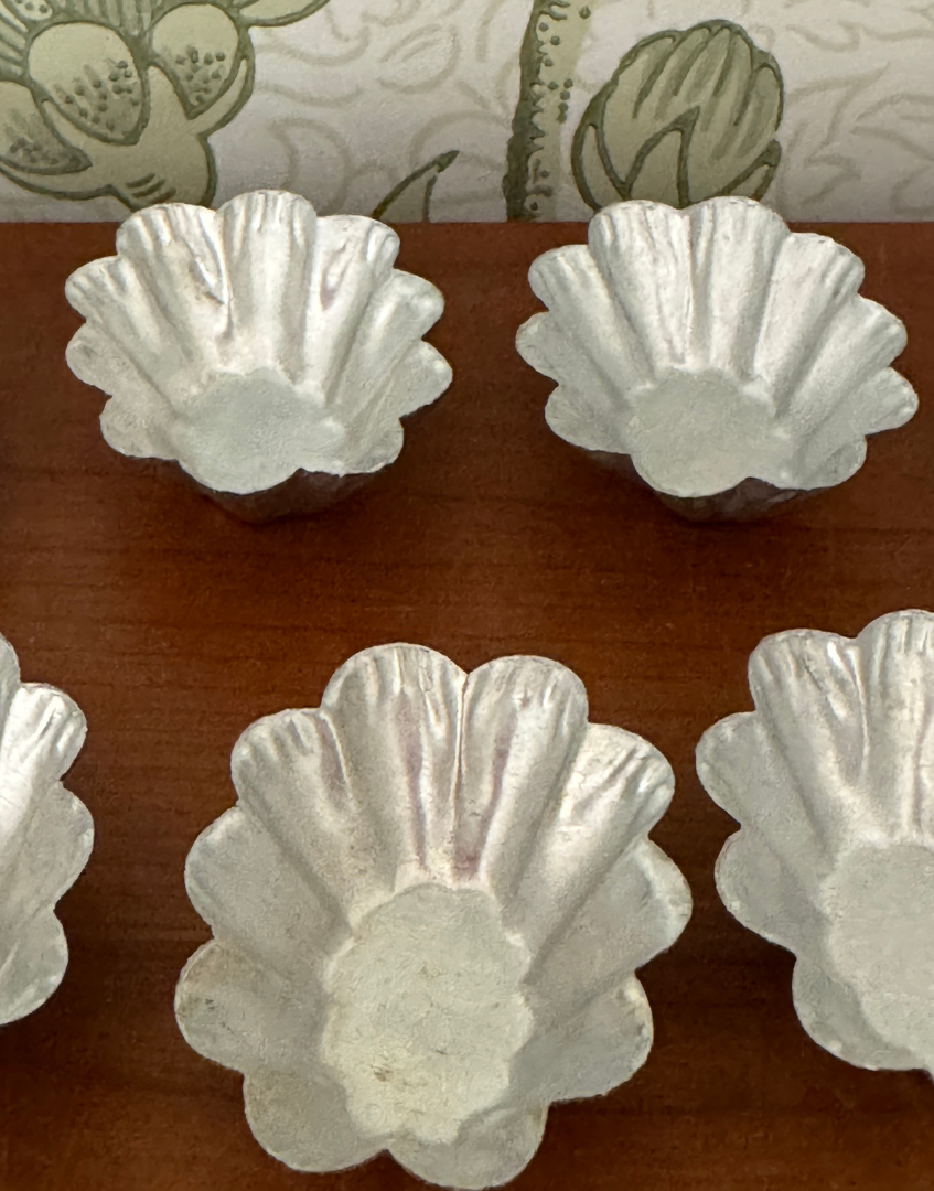 Close up of vintage fluted petit four moulds styled on a wooden shelf with other antique kitchenalia pieces