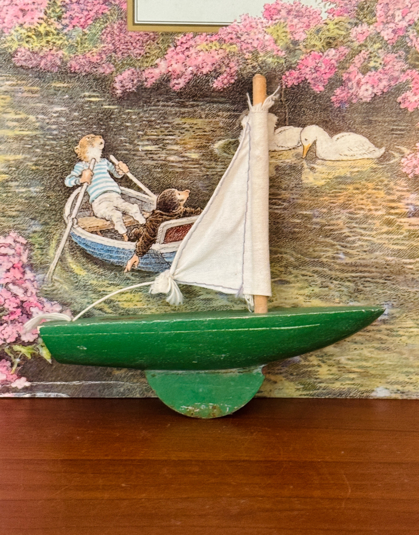 Miniature Star Yachts green pond yacht displayed on a wooden shelf alongside Wind in the Willows for a nostalgic countryside setting.