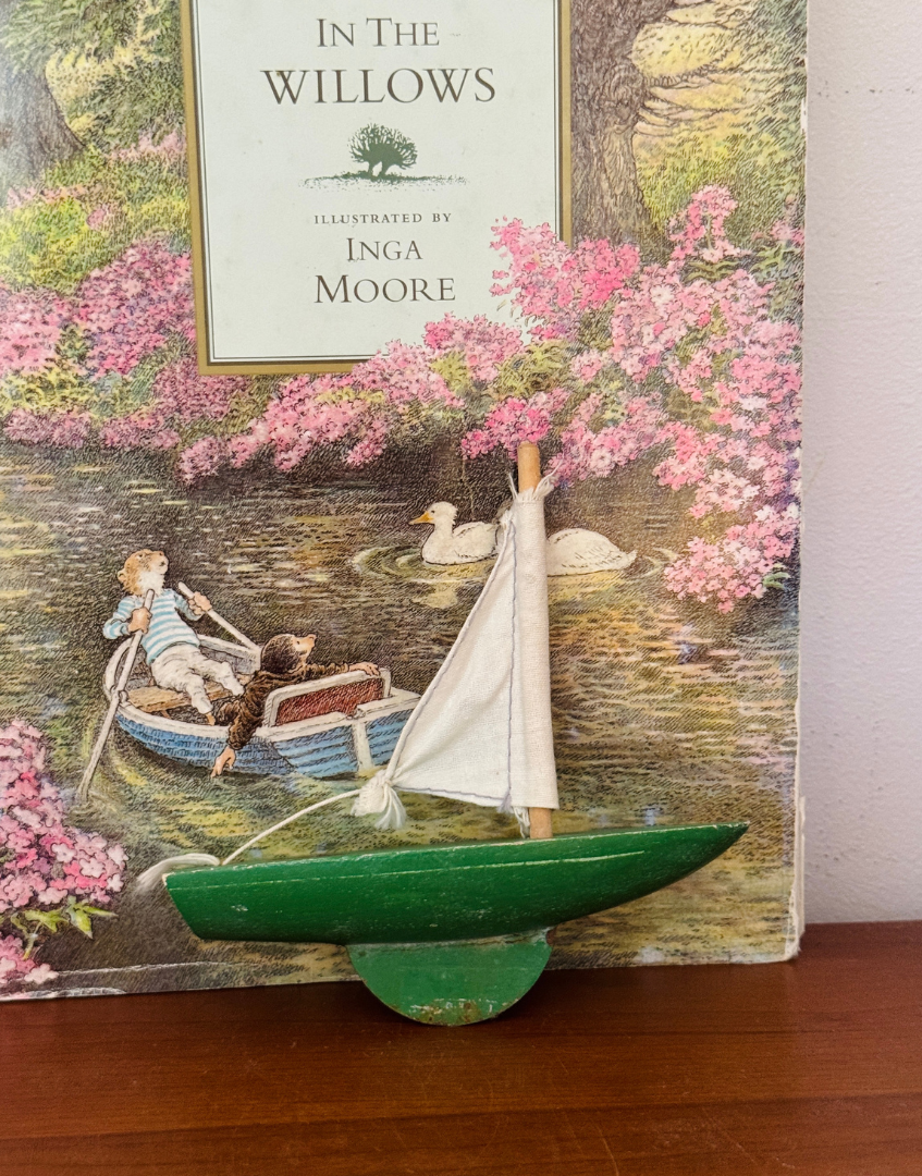 Vintage green Star Yachts pond yacht styled on a wooden shelf with a classic Wind in the Willows book cover.