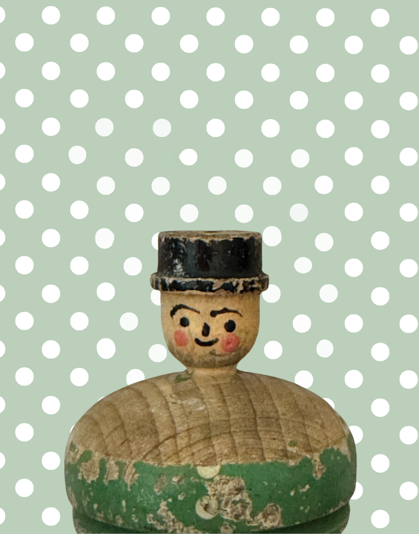 Close up of the hand carved gentleman’s painted facial features and bowler hat on the antique wooden spinning top.