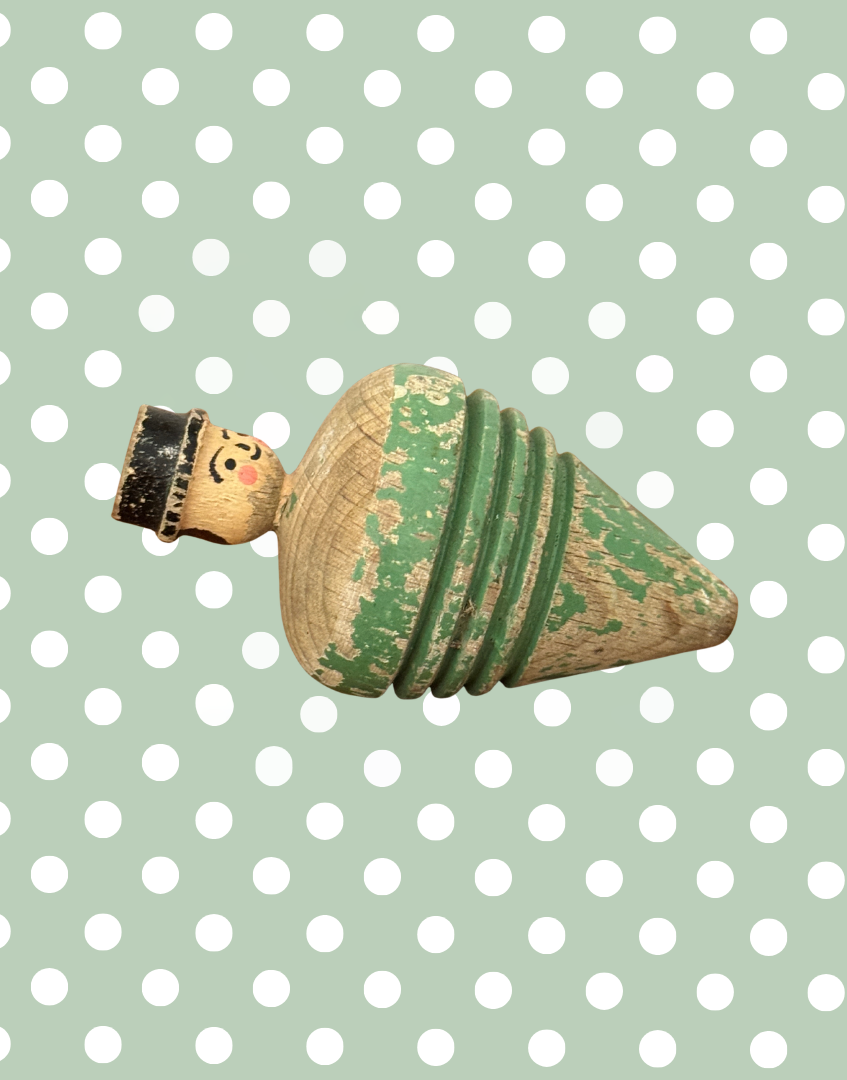 Left side view of antique carved gentleman spinning top showing the sculpted head, bowler hat and aged wooden surface.