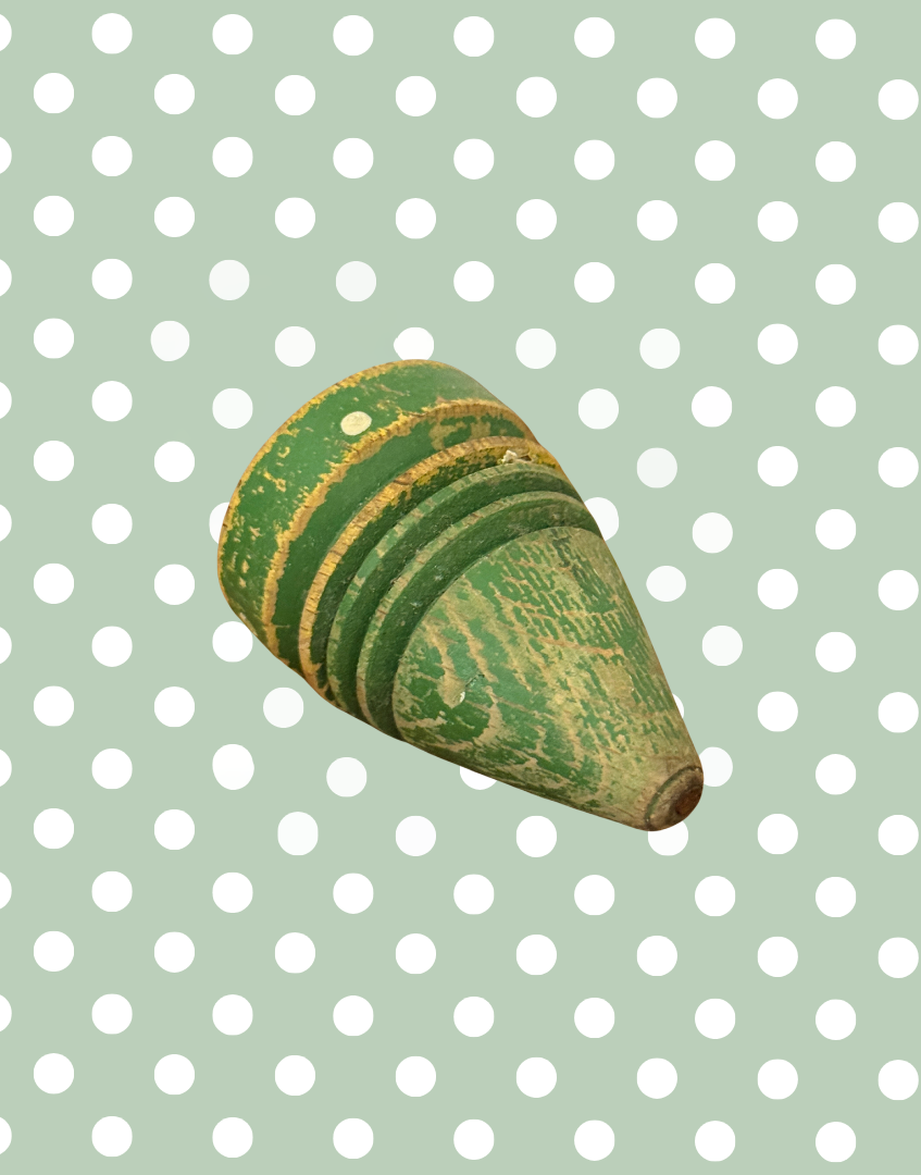 Side view of antique wooden spinning top with painted polka dot decoration and gently weathered surface.