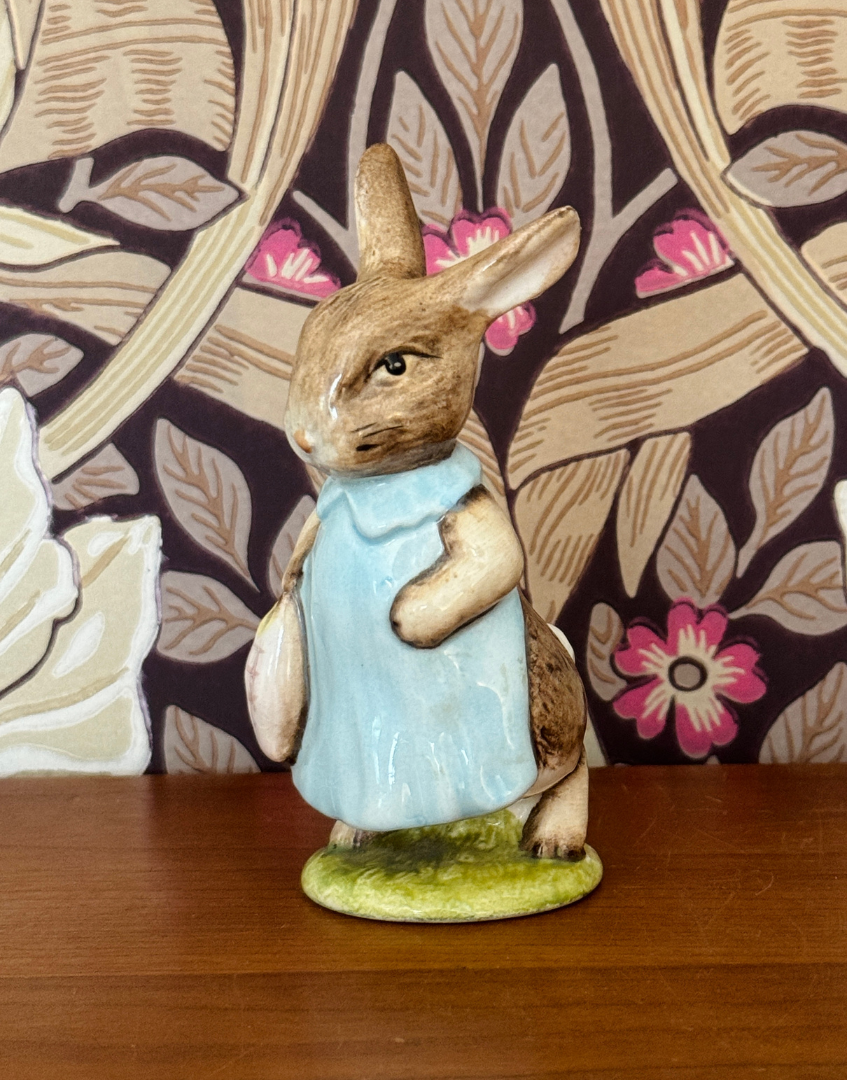 Beswick Mrs Flopsy Bunny Beatrix Potter figurine displayed on a wooden shelf against William Morris Pimpernel wallpaper.