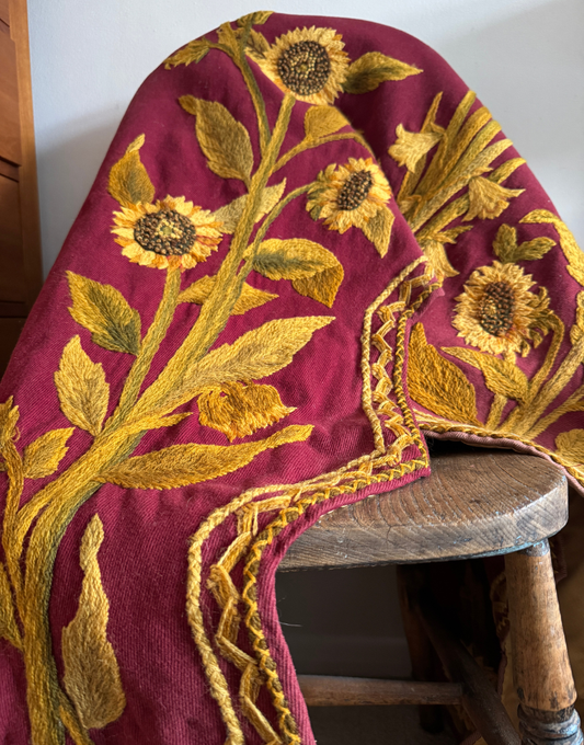 Antique Arts and Crafts crewelwork pelmet draped over an antique chair, showing its rich plum ground and large scale floral embroidery.