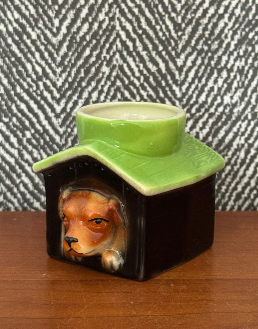 Vintage Tony Wood dog in kennel egg cup on a wooden surface against black and white patterned fabric.