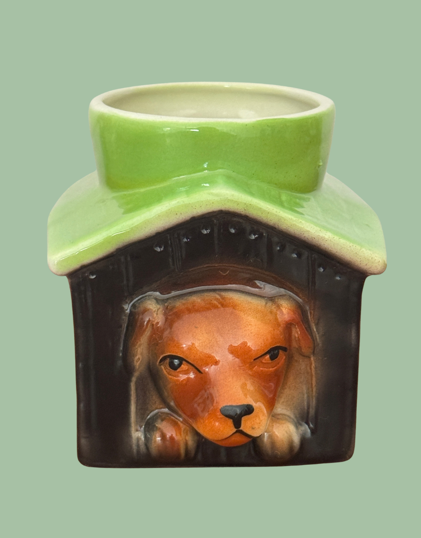 Close front view of Tony Wood dog in kennel egg cup showing the brown dog’s face and paws beneath an apple green roof.
