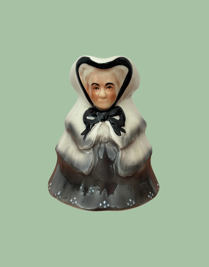 Front view of Tony Wood Little Old Lady milk jug showing her painted face, cream hood, black bow and clasped hands.