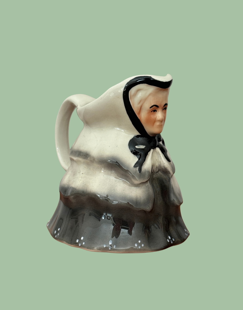 Side view of Tony Wood Little Old Lady milk jug showing her profile, cream handle and moulded folds in the grey clothing.