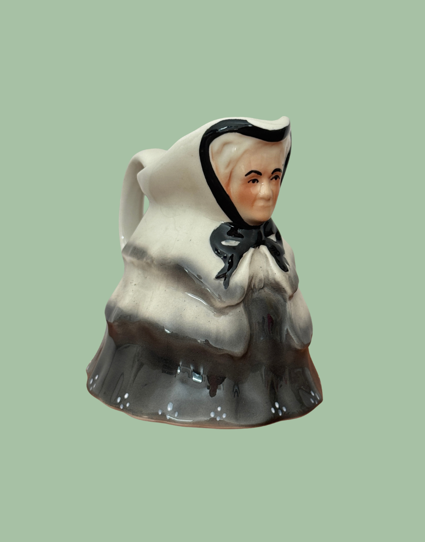 Vintage Tony Wood Little Old Lady milk jug in black, grey and cream, shown at an angle with its curved handle visible.
