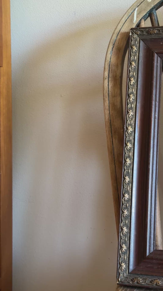 Video showing antique decorative wood and metal picture frame with aged finish and ornate detailing on vintage wooden chair.
