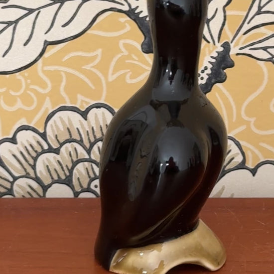 Video showing the vintage black pie bird from several angles, including its open beak, curved body and earthy olive log base.