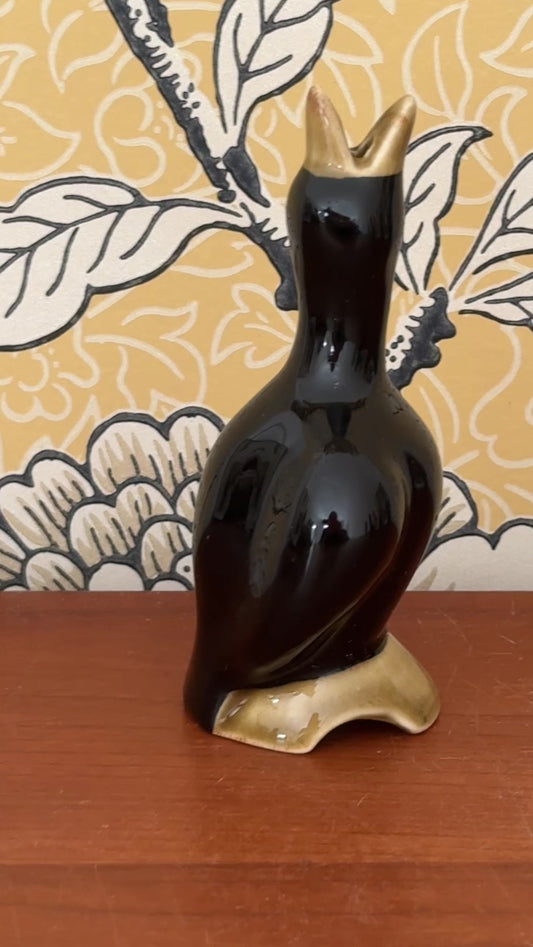 Video showing the vintage black pie bird from several angles, including its open beak, curved body and earthy olive log base.