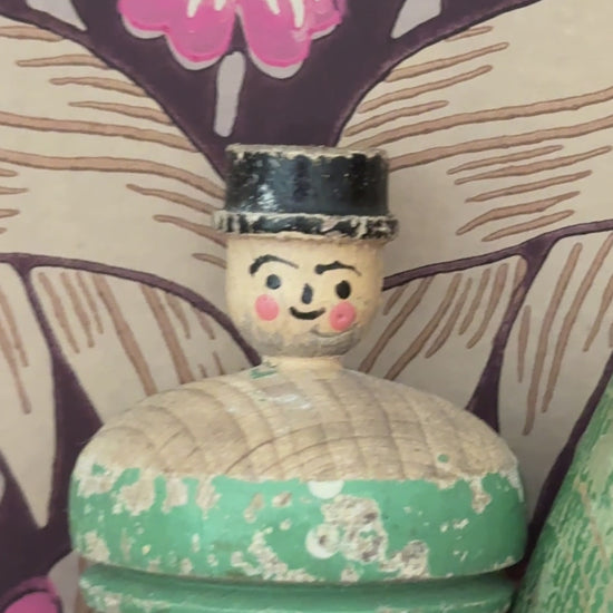 Pair of antique wooden spinning tops styled on a wooden shelf against William Morris Pimpernel wallpaper, featuring a carved gentleman and painted polka dot design.