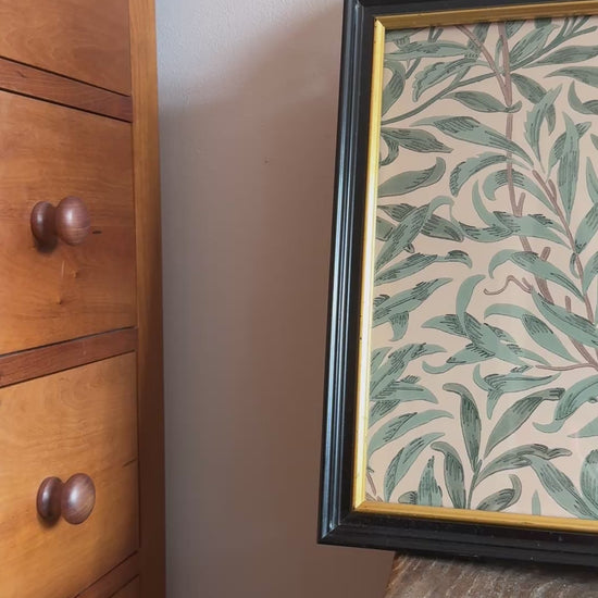 Black and gold almost square framed William Morris Willow Boughs Privet bitanical print placed on seat of an antique wooden chair.